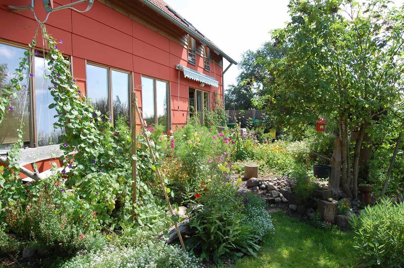 Rote Hausfassade mit großen Holzfenstern, davor ein blühender Garten